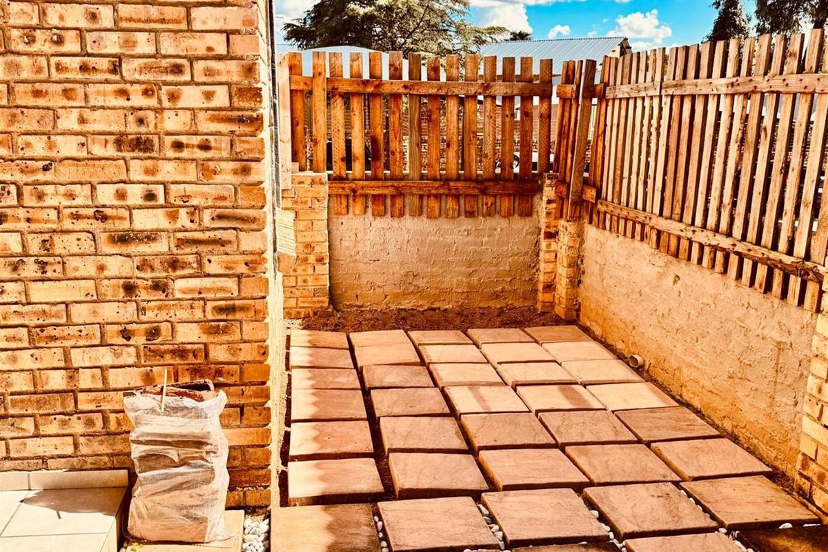 A private rear courtyard featuring a paved patio area enclosed by brick walls and a wooden perimeter fence.