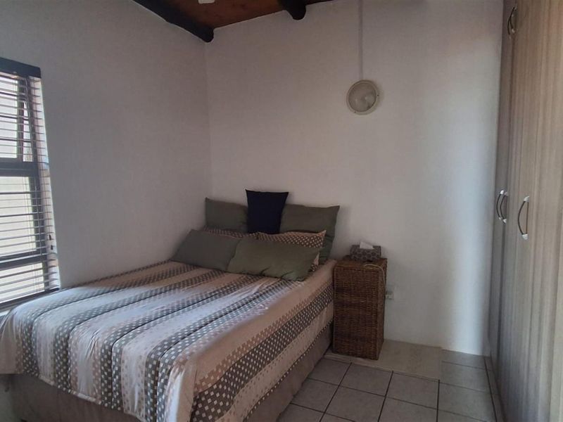 A functional bedroom featuring tiled flooring, built-in wooden cupboards, and a window with fitted blinds, providing a practical living space.