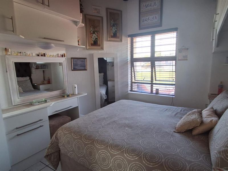 A compact bedroom featuring built-in cabinetry, a vanity unit, and a window with fitted blinds, providing functional storage and natural light.