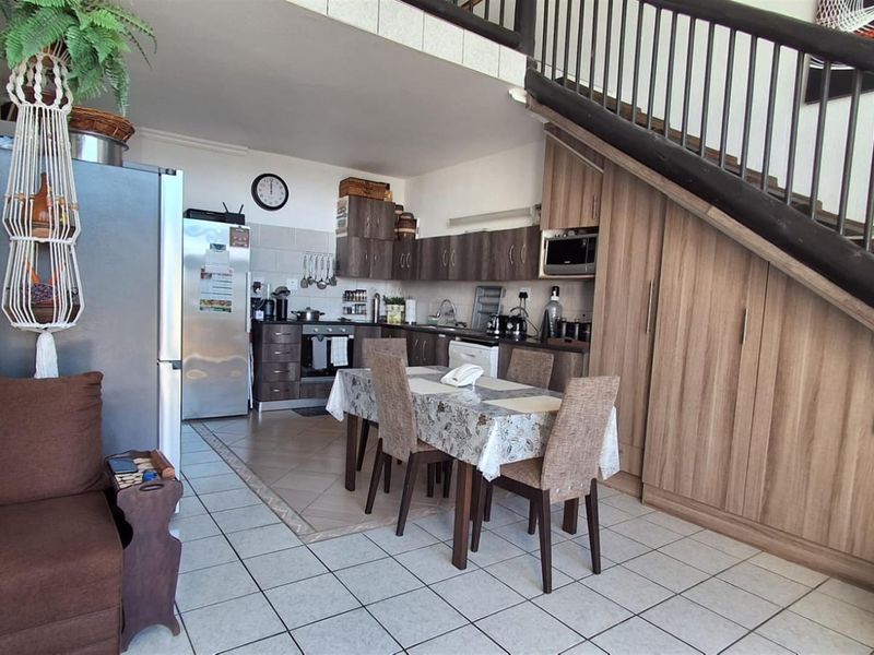 Open-plan kitchen and dining area featuring wood-look cabinetry, tiled flooring, and a staircase with a dark metal railing.
