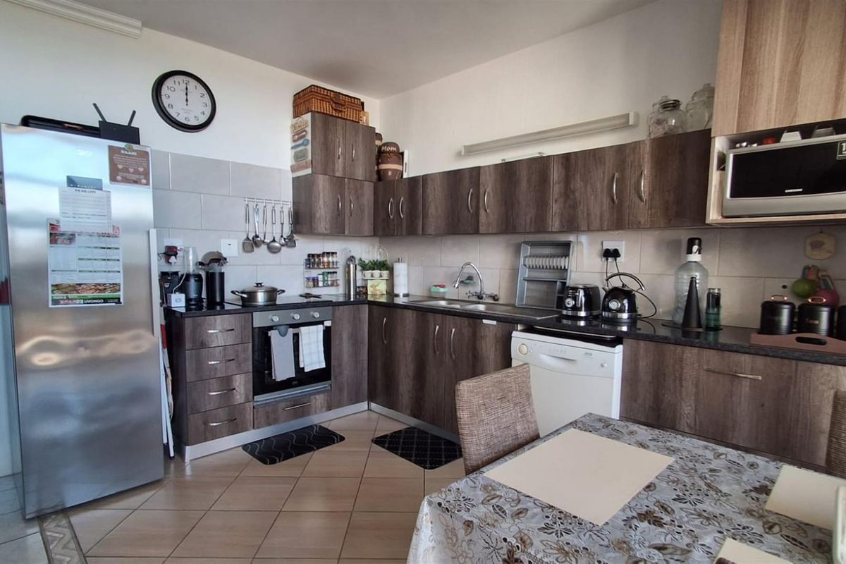 A functional kitchen featuring wood-grain cabinetry, dark countertops, tiled backsplash, and integrated appliances, offering a practical layout for daily meal preparation.
