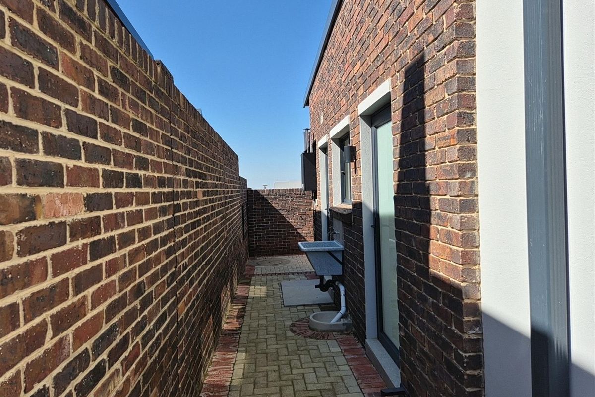 A narrow side passage featuring brick paving, a wall-mounted utility sink, and brick boundary walls.