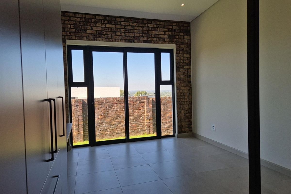 A bright bedroom featuring large sliding glass doors, a rustic exposed brick feature wall, and modern neutral floor tiles.