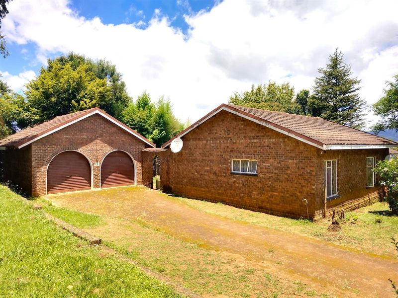 A detached brick house featuring a double garage and a paved driveway, set within a spacious garden area.