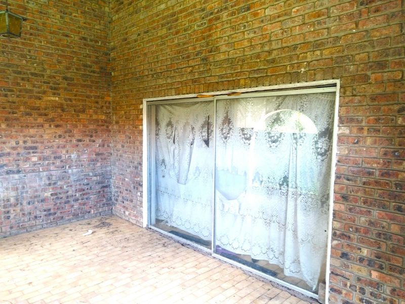 A covered patio area featuring exposed brick walls and paved flooring, providing direct access to the interior through a sliding glass door.