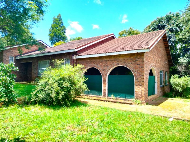 A traditional face-brick house featuring arched patio openings, a pitched tiled roof, and established garden surroundings.