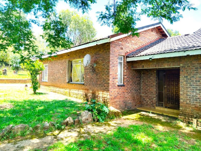 A single-story face-brick house exterior featuring a covered entrance, tiled roof, and surrounding garden area.