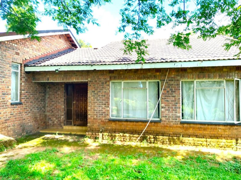A classic face-brick exterior facade featuring a tiled roof, large windows, and a covered entrance area set within a garden.