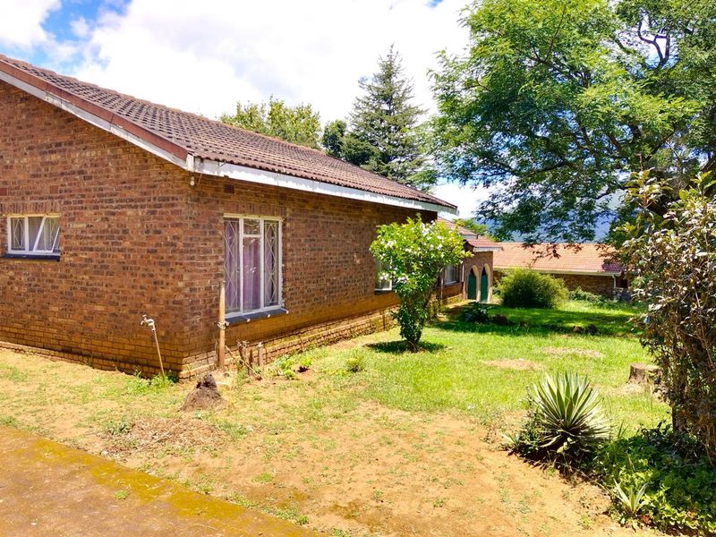 A view of the rear exterior of a brick house featuring a tiled roof, metal-framed windows, and a spacious garden area.