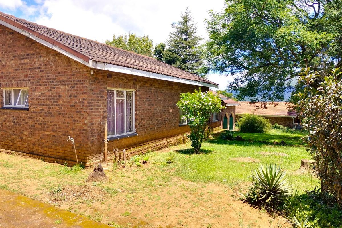 A view of the rear exterior of a brick house featuring a tiled roof, metal-framed windows, and a spacious garden area.