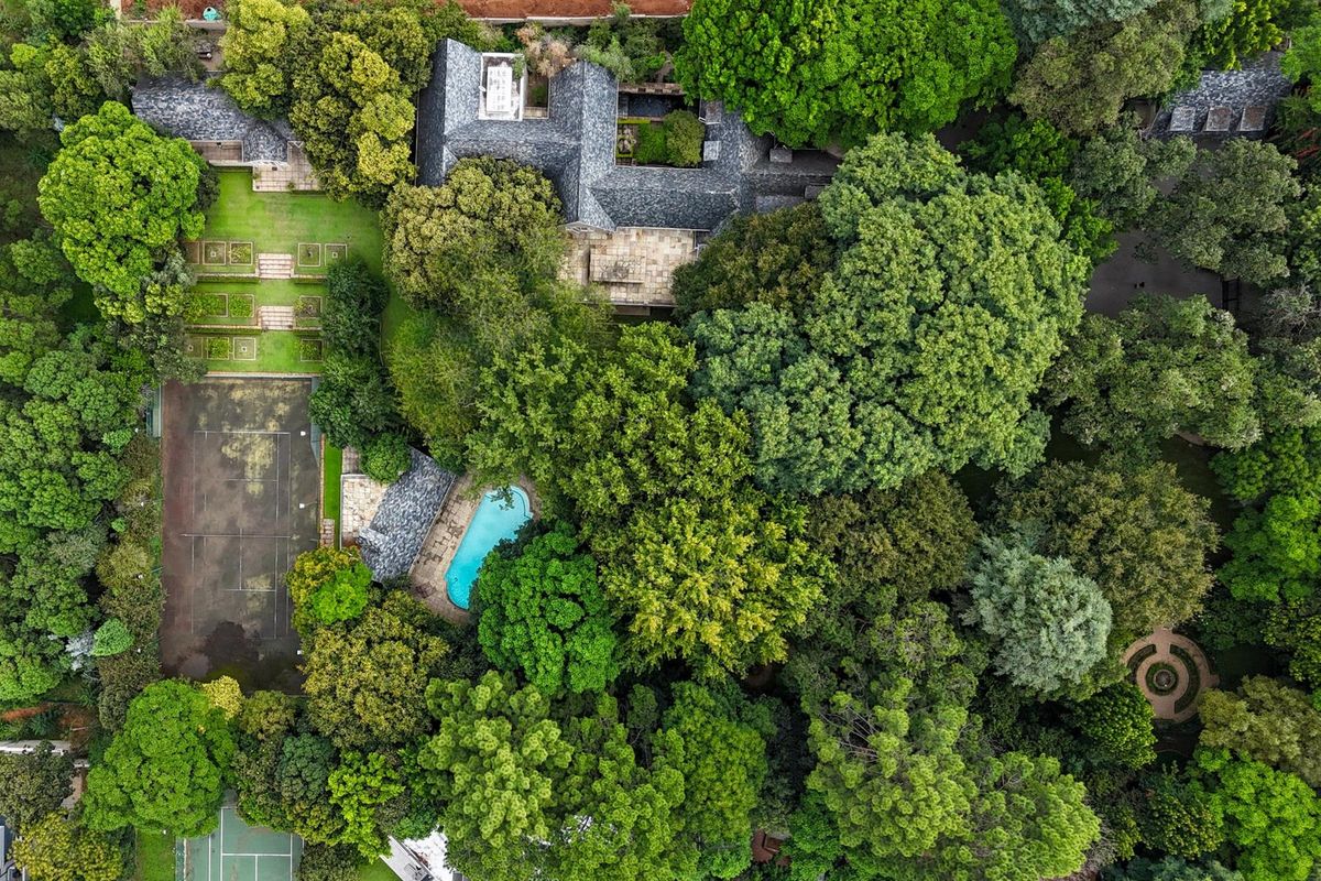 Aerial view of a large residential property featuring a swimming pool, tennis court, landscaped gardens, and mature trees surrounding the main dwelling.