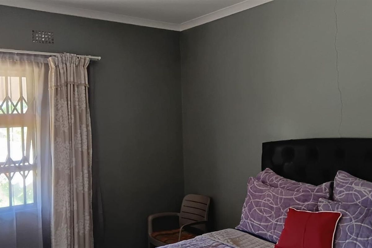 A bedroom featuring dark grey walls, a window with security bars, and a visible vertical crack in the wall.