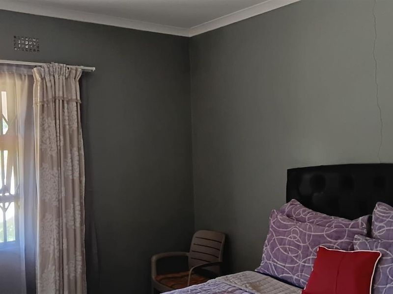 A bedroom featuring dark grey walls, a window with security bars, and a visible vertical crack in the wall.