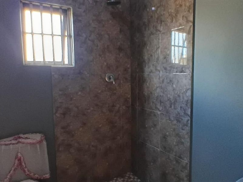 A bathroom featuring a shower area with brown tiled walls, a small window with security bars, and painted wall finishes.
