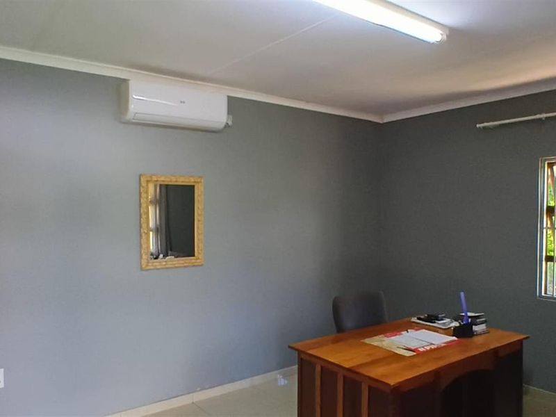 A functional office space featuring a wall-mounted air conditioning unit, tiled flooring, and a window with security bars.