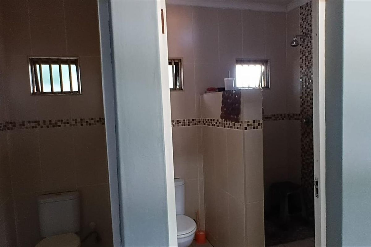 A functional bathroom featuring a tiled shower enclosure, toilet, and mosaic tile accents, providing a practical layout for daily use.