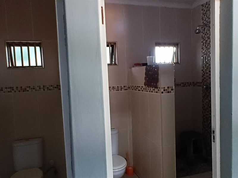 A functional bathroom featuring a tiled shower enclosure, toilet, and mosaic tile accents, providing a practical layout for daily use.