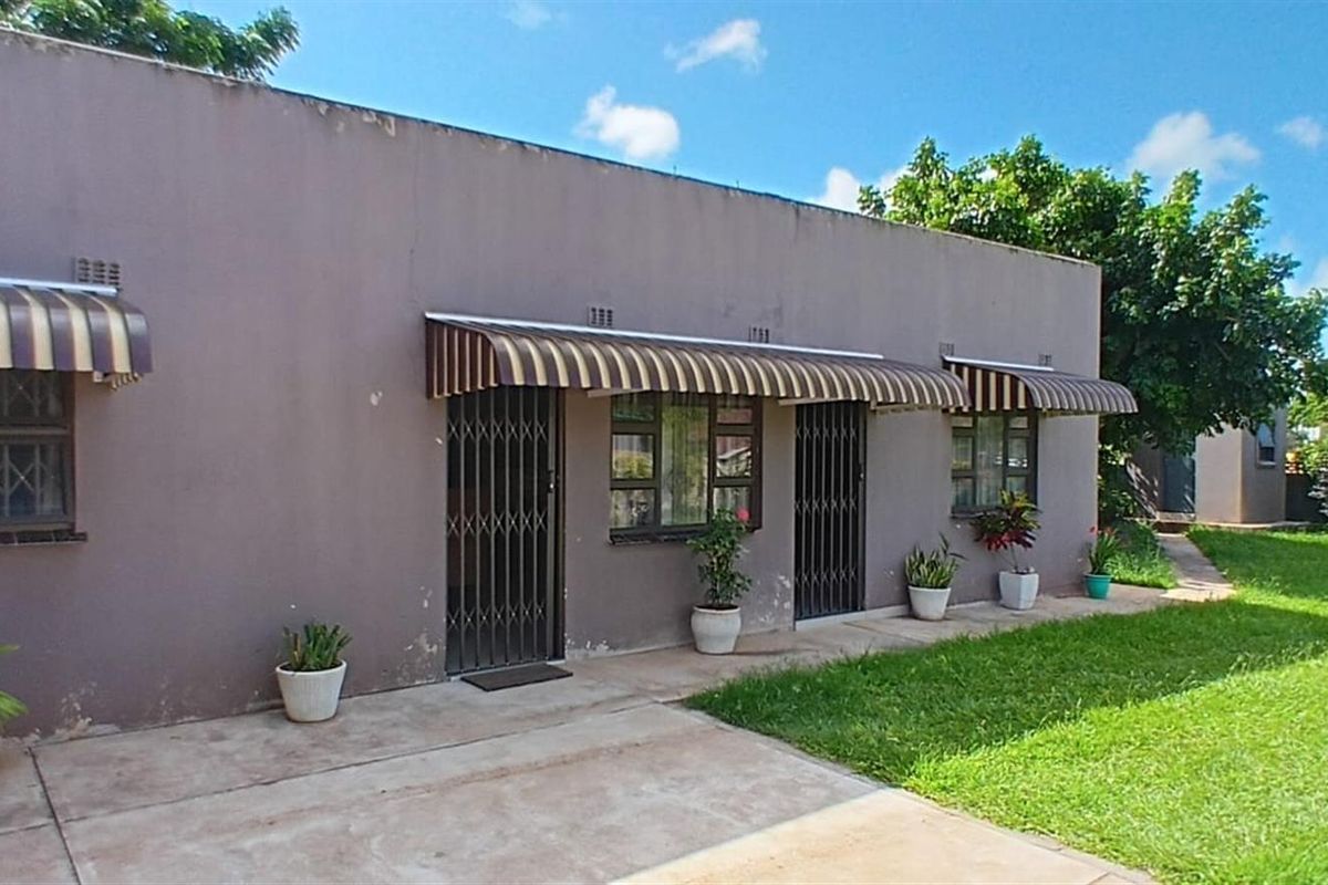 Rear exterior view of the house featuring a concrete patio, lawn area, and protective window awnings with security gates.