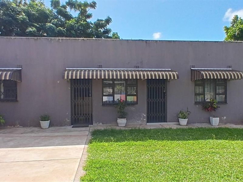 Exterior view of a single-story residential property featuring a concrete driveway, lawn, and metal security gates over the entrance and window openings.