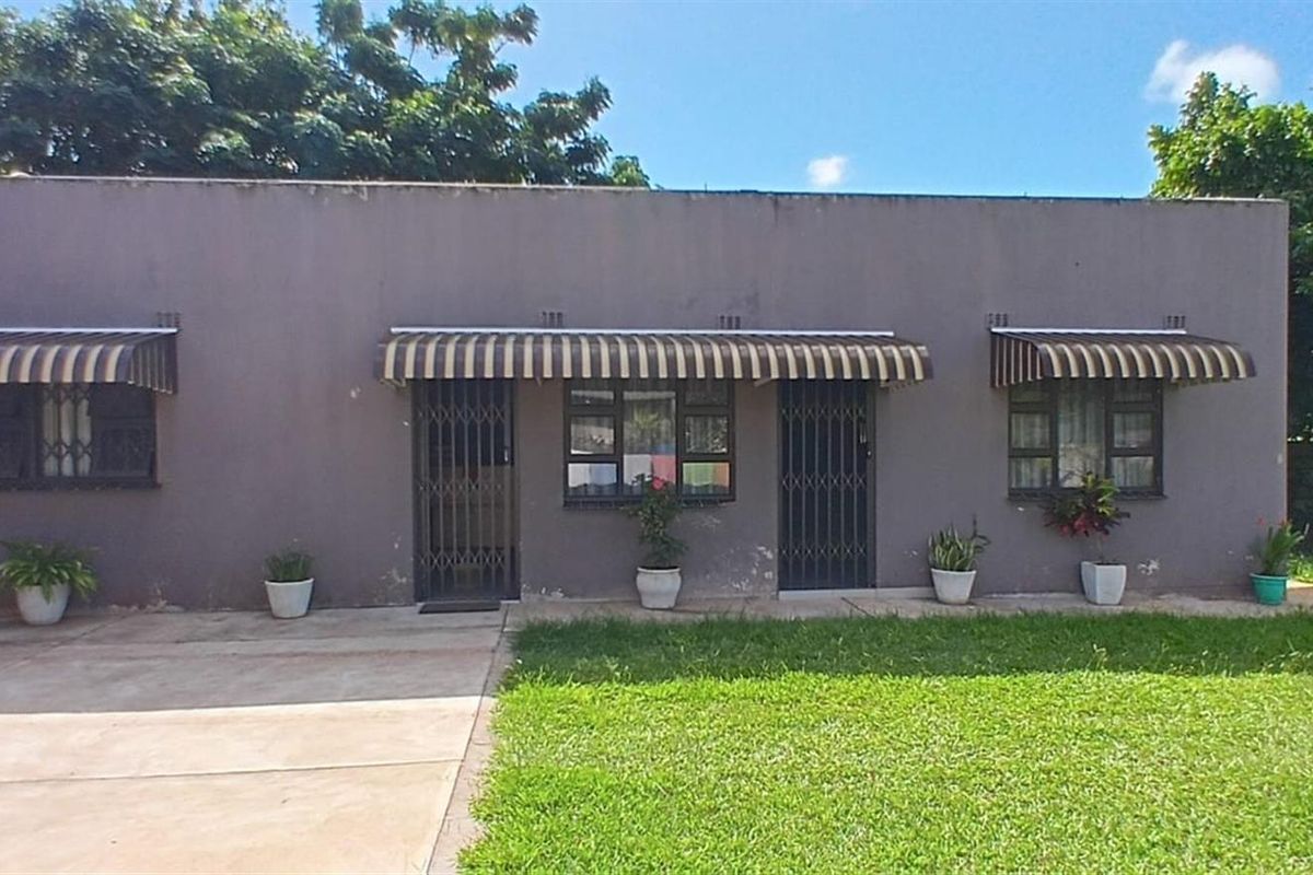 Exterior view of a single-story residential property featuring a concrete driveway, lawn, and metal security gates over the entrance and window openings.