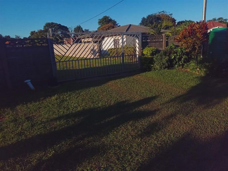 A view of the front garden area featuring a metal driveway gate, perimeter walling, and established landscaping.