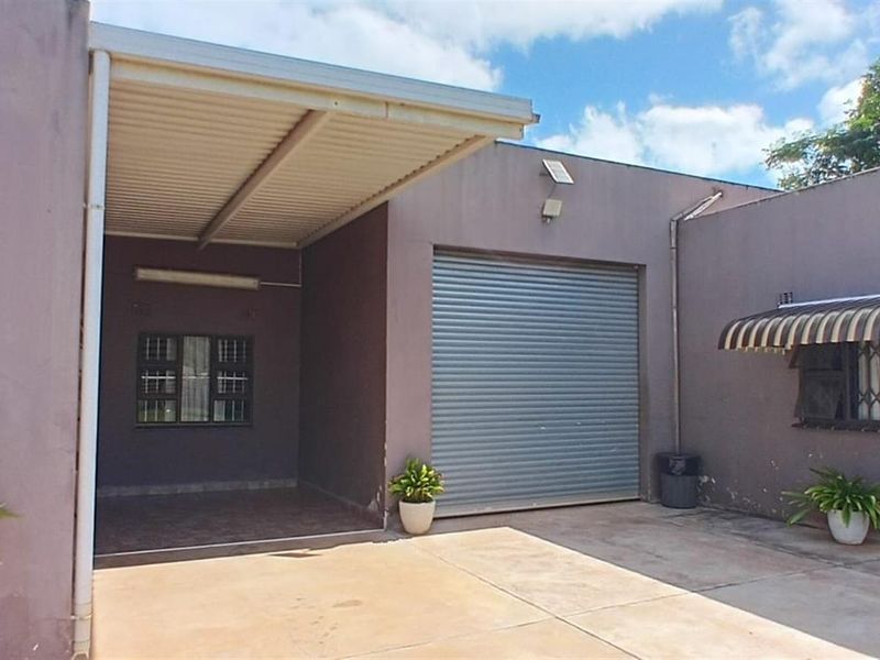 Exterior view of the property featuring a covered carport, a secure roller shutter garage door, and paved driveway area.
