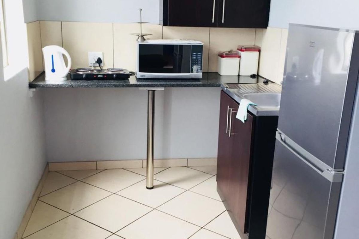 Compact kitchen area featuring dark cabinetry, granite-look countertops, tiled flooring, and a stainless steel sink.