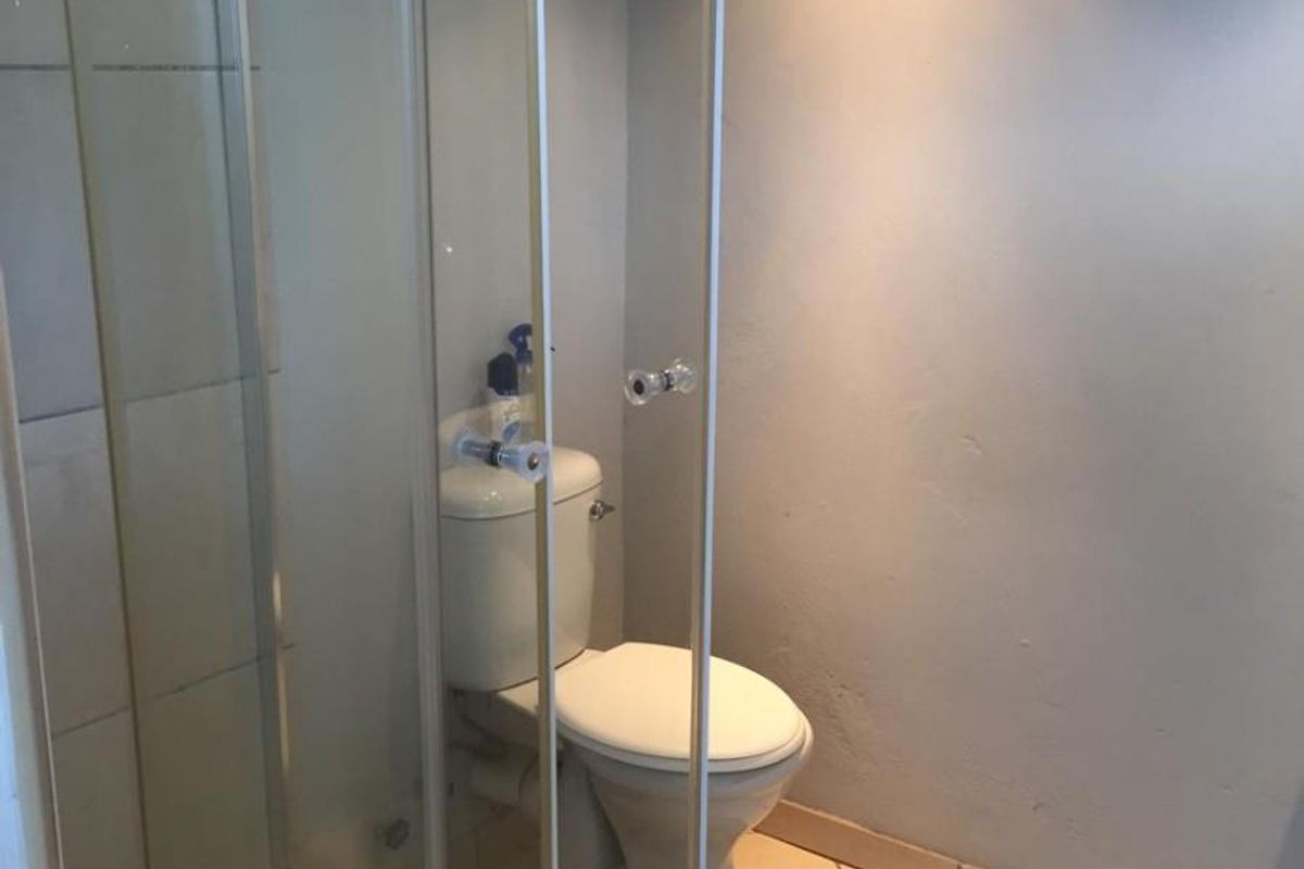 A functional bathroom featuring a glass-enclosed shower cubicle and a standard white toilet with tiled flooring.