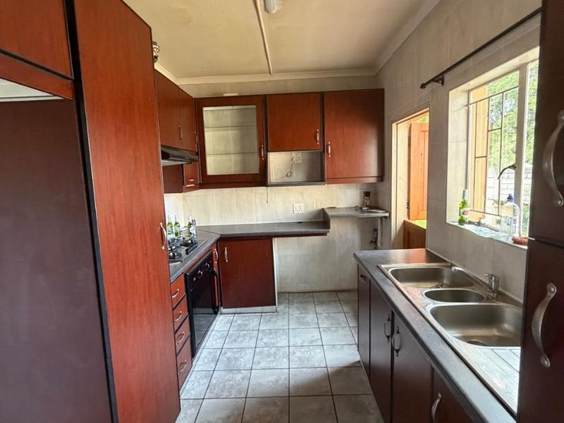 A functional kitchen featuring dark wood cabinetry, a double stainless steel sink, built-in oven, and tiled flooring, offering potential for a modern renovation.