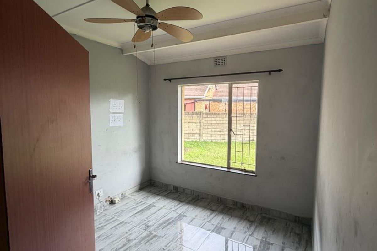 An empty bedroom featuring tiled flooring, a ceiling fan, and a window with security bars, awaiting personal touches and cosmetic updates.