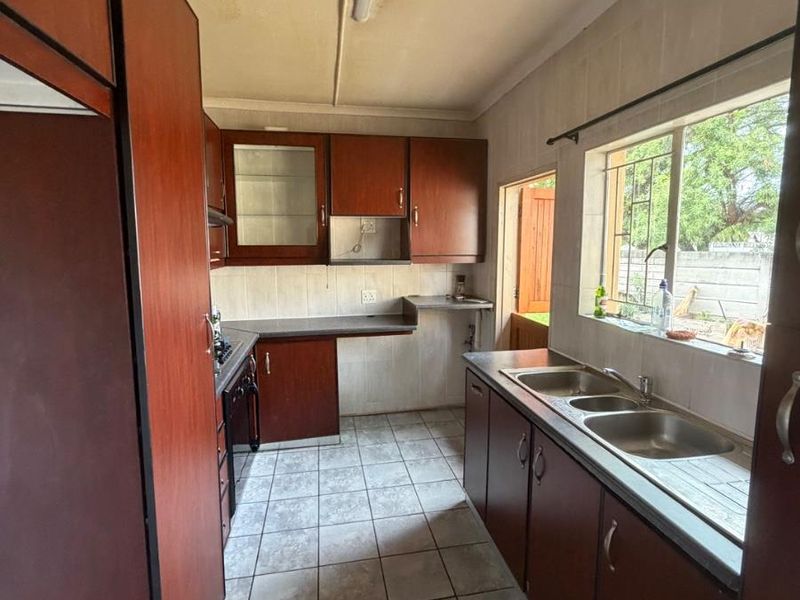 A functional kitchen featuring dark wood-look cabinetry, tiled flooring, a double stainless steel sink, and built-in cooking appliances, offering potential for modern updates.
