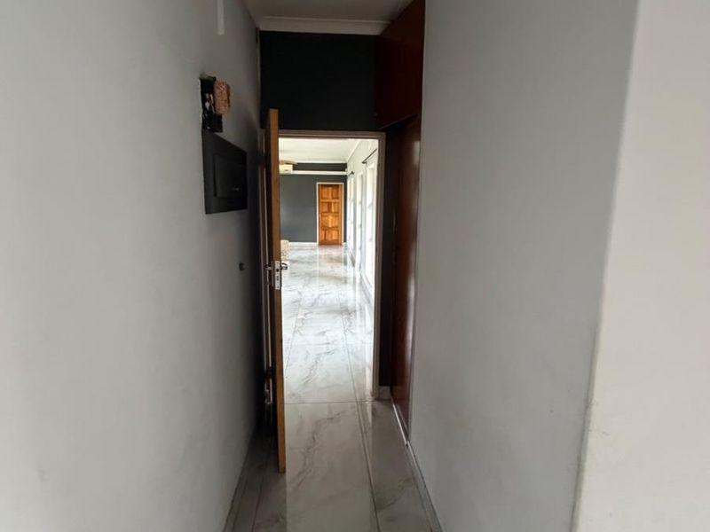 A narrow interior hallway featuring light-colored tiled flooring and a built-in storage cupboard, leading into an adjacent living space.