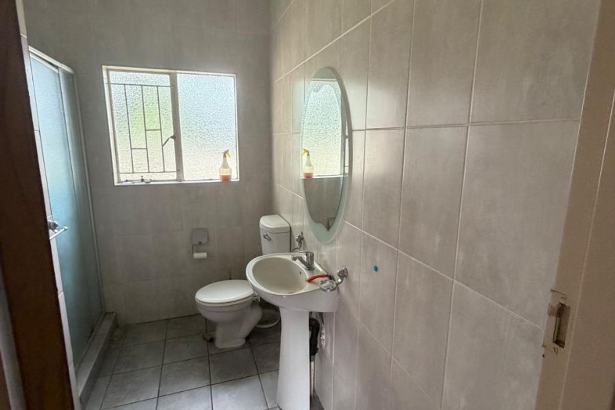 A functional bathroom featuring a pedestal sink, toilet, and a glass-enclosed shower with neutral floor-to-ceiling wall tiles.