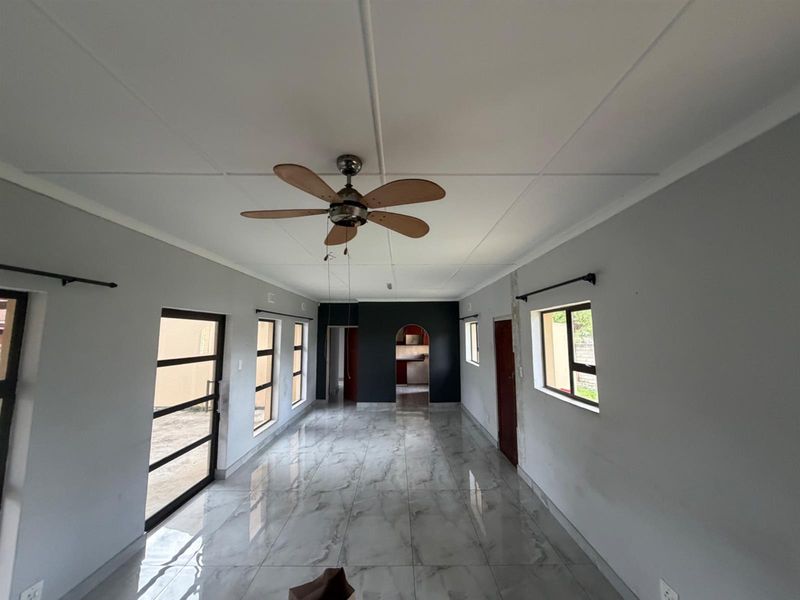 Spacious open-plan living area featuring modern marble-look floor tiles, a ceiling fan, and an arched entryway leading to the kitchen.