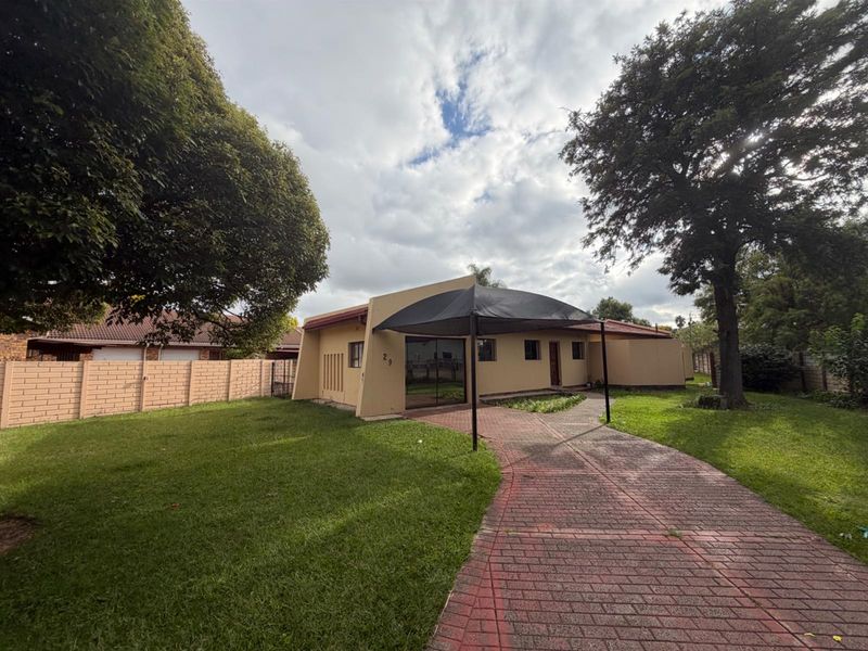 Front exterior view of the property featuring a paved driveway, shade sail structure, and established garden with brick boundary walling.