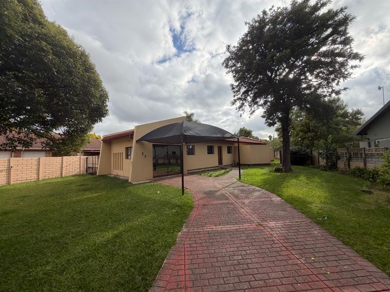 Front exterior view of the property featuring a paved driveway, established lawn, and a shade sail structure over the entrance area.