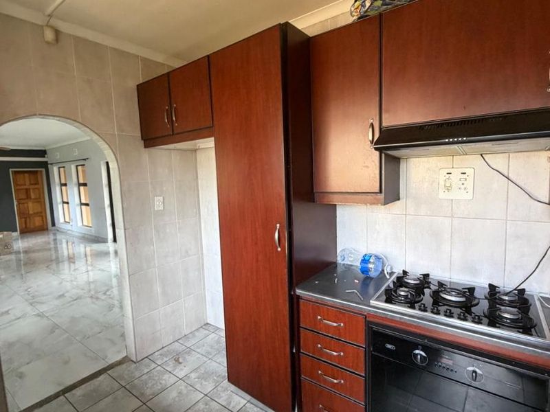 A functional kitchen featuring dark wood cabinetry, a built-in gas hob, oven, and extractor fan, with tiled flooring and an arched entryway to the living area.