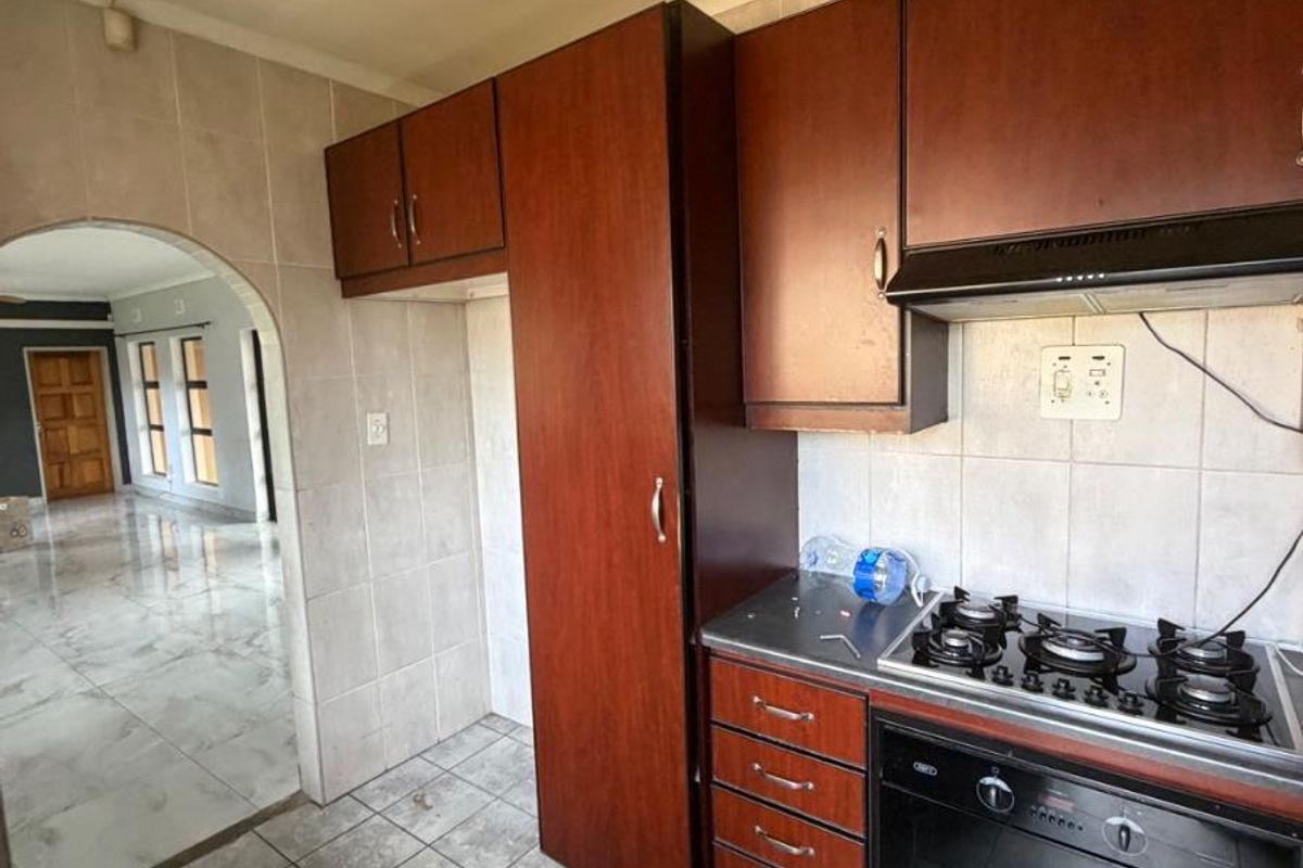 A functional kitchen featuring dark wood cabinetry, a built-in gas hob, oven, and extractor fan, with tiled flooring and an arched entryway to the living area.