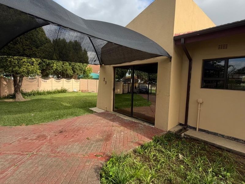 A paved outdoor patio area featuring a shade sail, sliding door access, and a surrounding garden with a precast boundary wall.
