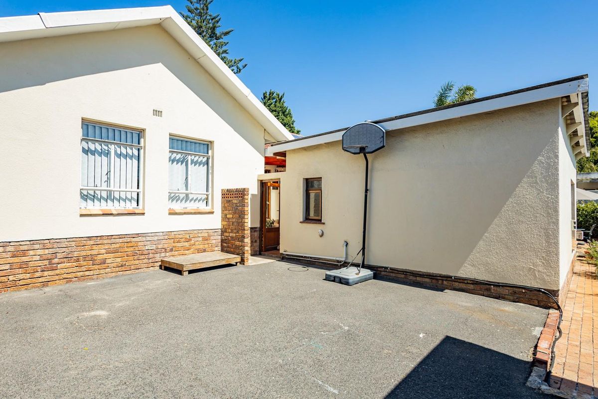 A rear exterior view of the house featuring a paved courtyard area, brick accents, and security bars on the windows.