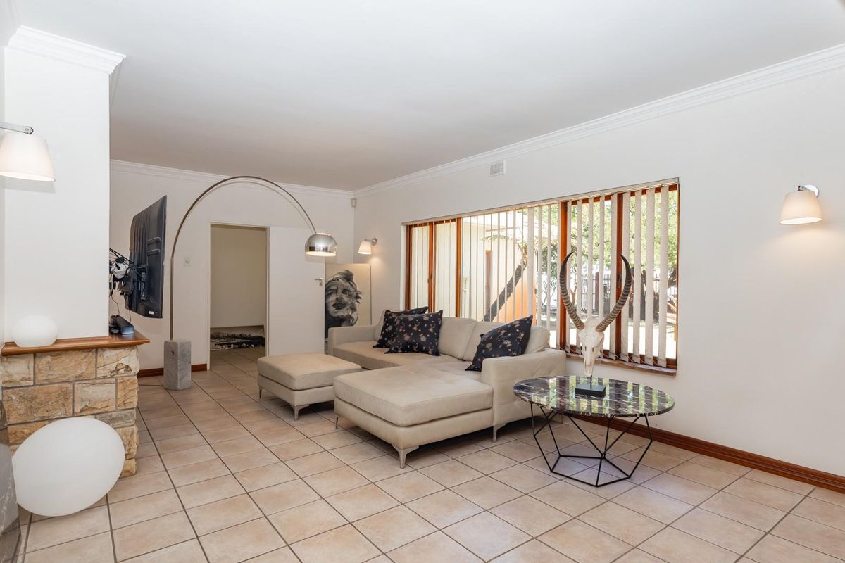 A spacious living room featuring neutral floor tiles, a stone-clad fireplace feature, and large windows with vertical blinds, offering a bright and functional living space.