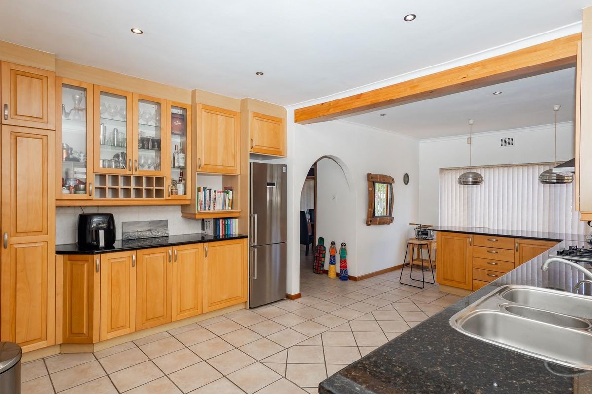Spacious kitchen featuring light wood cabinetry, dark granite countertops, double stainless steel sink, and integrated gas hob, flowing into an open-plan living area.