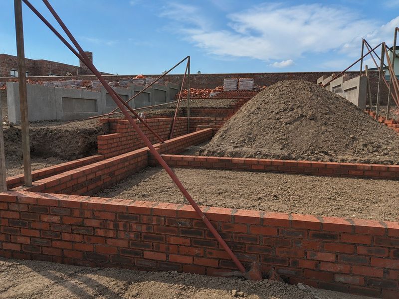A construction site showing the brick foundation walls and concrete boundary wall of a property currently under development.