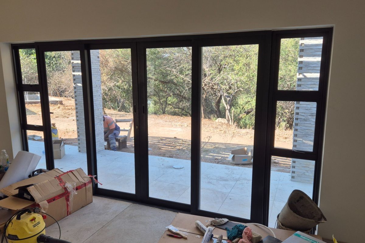 Spacious living area featuring modern black aluminium stacker doors opening onto a patio with views of the surrounding natural landscape.