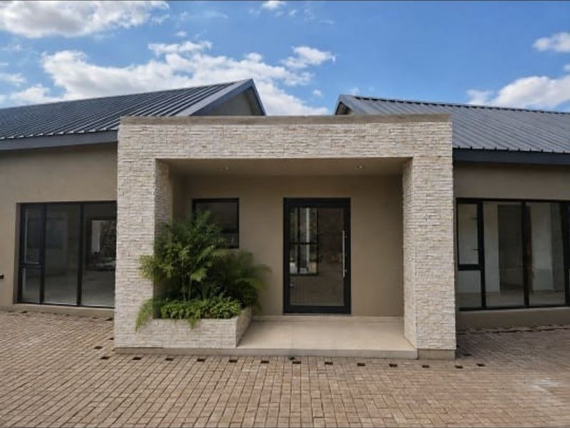 Modern front entrance featuring stone cladding, paved driveway, and large aluminium-framed windows under a contemporary metal roof.