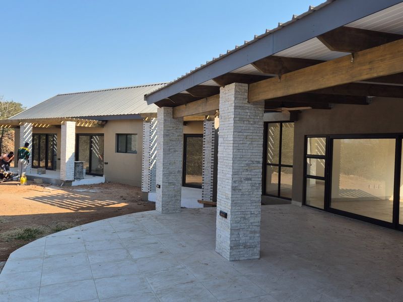 Spacious covered patio featuring stone-clad pillars and timber beams, providing seamless indoor-outdoor flow through large sliding glass doors.