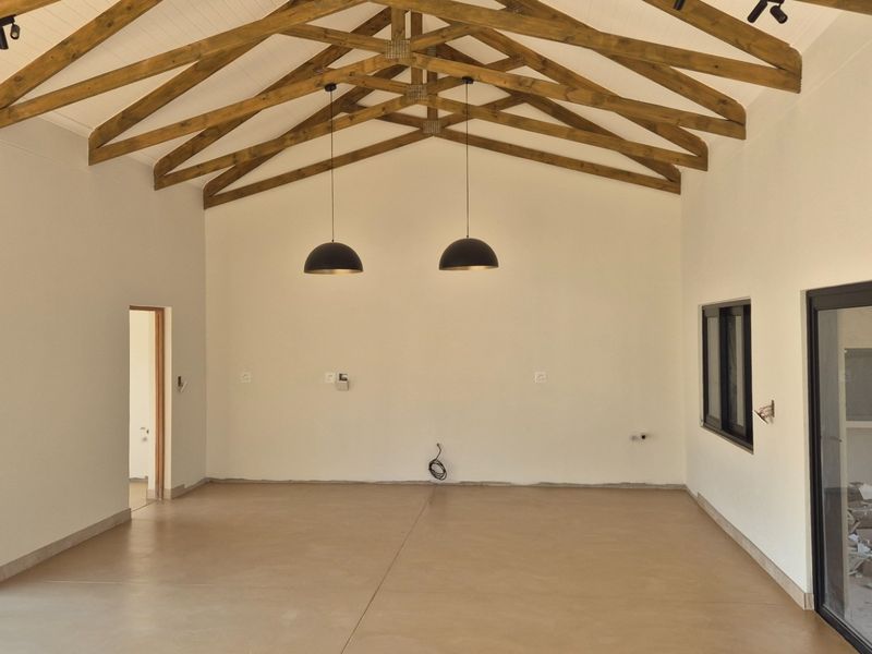 Spacious open-plan living area featuring a high vaulted ceiling with exposed timber trusses, polished concrete floors, and modern pendant lighting.
