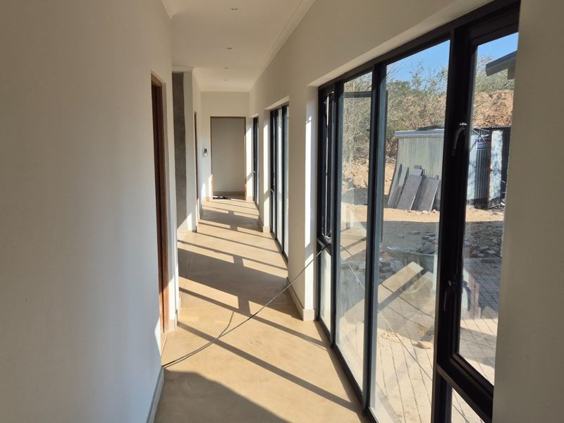 A bright, empty hallway featuring large aluminium-framed windows that provide ample natural light and views of the exterior area.