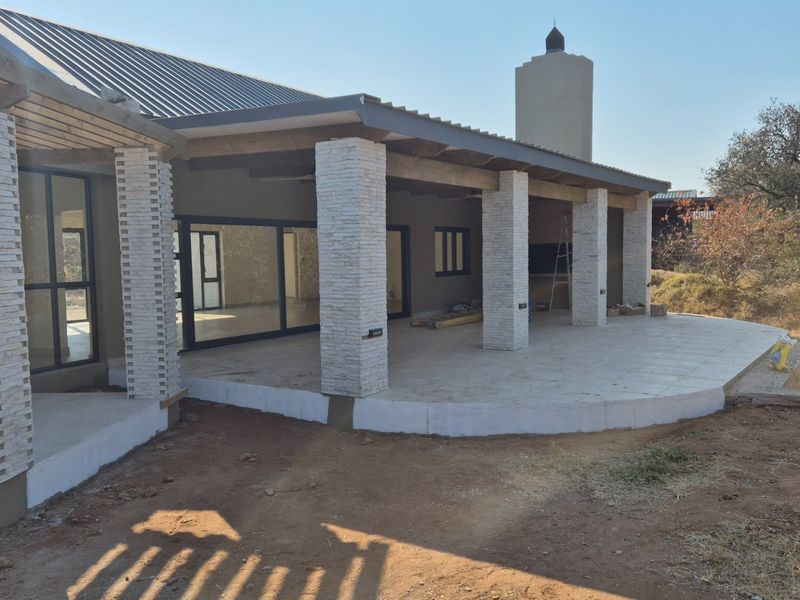 Spacious covered patio featuring stone-clad pillars, tiled flooring, and direct access to the interior through large sliding glass doors.