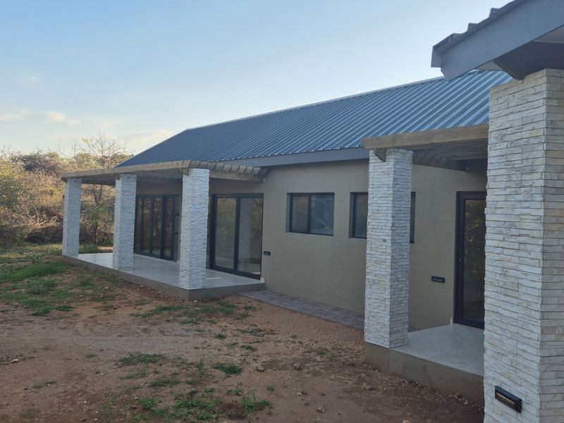 A modern rear exterior view featuring a covered patio with stone-clad pillars, timber pergola, and large sliding glass doors leading into the home.